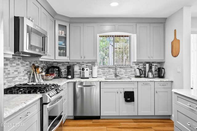 kitchen with stainless steel appliances, gray cabinets, a sink, and tasteful backsplash