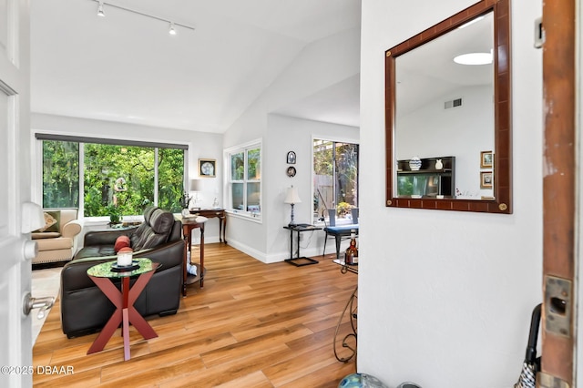 living room featuring visible vents, baseboards, rail lighting, light wood finished floors, and vaulted ceiling