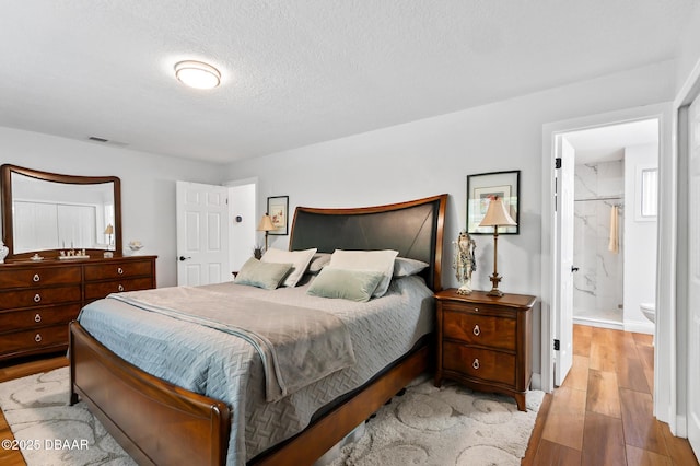 bedroom featuring a textured ceiling, ensuite bath, wood finished floors, and visible vents