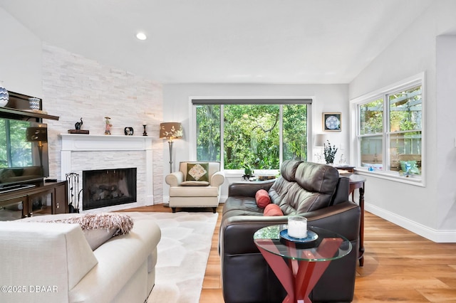 living area with baseboards, a stone fireplace, a wealth of natural light, and wood finished floors
