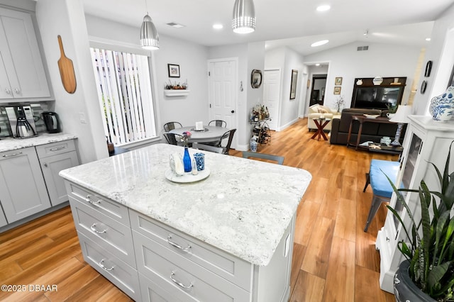 kitchen with a kitchen island, decorative light fixtures, light stone countertops, and light wood-style flooring