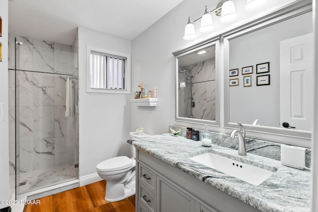 bathroom with a marble finish shower, vanity, toilet, and wood finished floors