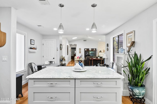 kitchen featuring hanging light fixtures, visible vents, light stone counters, and light wood-type flooring