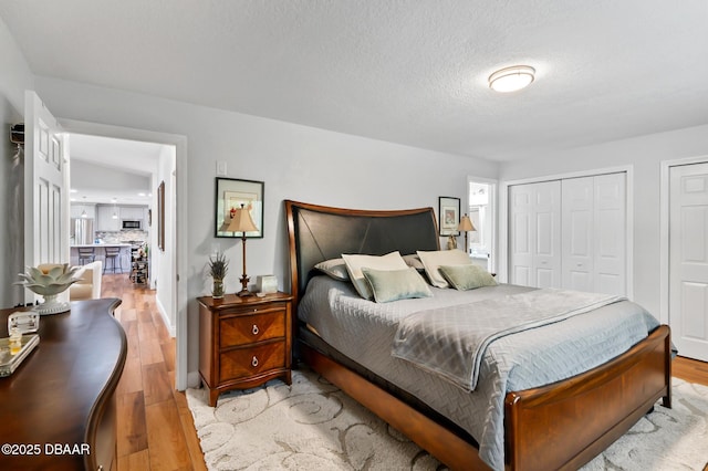 bedroom with two closets, a textured ceiling, and light wood-type flooring