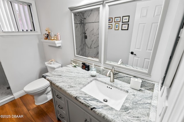 bathroom featuring vanity, toilet, a marble finish shower, baseboards, and wood finished floors