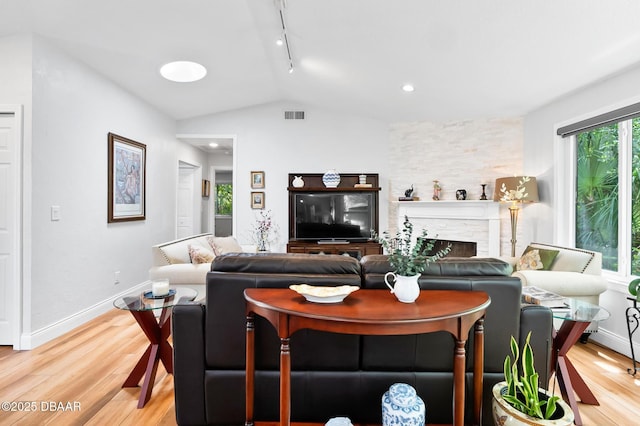 living area with a fireplace, rail lighting, light wood-style flooring, vaulted ceiling, and visible vents