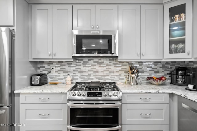 kitchen with glass insert cabinets, light stone counters, backsplash, and stainless steel appliances