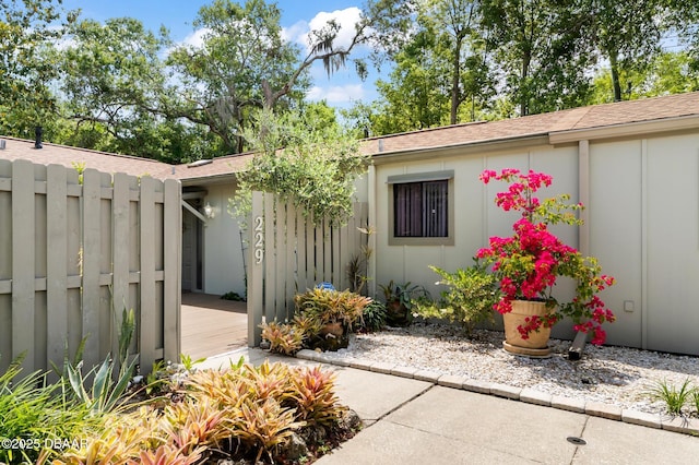 entrance to property featuring board and batten siding, roof with shingles, and fence