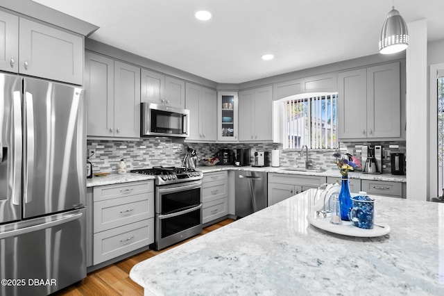 kitchen with light stone countertops, appliances with stainless steel finishes, a sink, gray cabinets, and decorative backsplash
