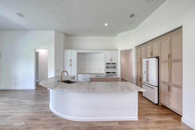 kitchen with a kitchen island with sink, light wood-type flooring, sink, and high end white fridge