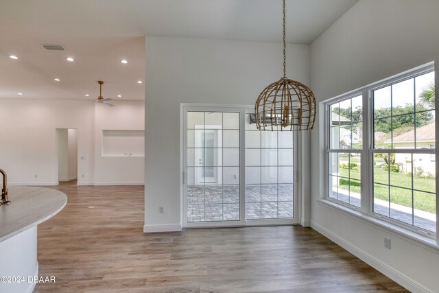 unfurnished dining area with a towering ceiling, light wood-type flooring, and ceiling fan with notable chandelier