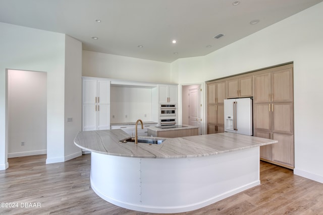 kitchen featuring stainless steel double oven, high end white fridge, light wood-type flooring, a large island, and sink