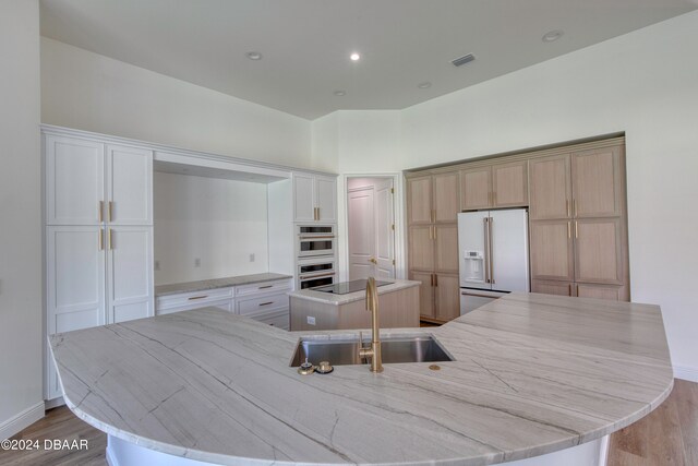 kitchen with sink, a spacious island, double oven, light wood-type flooring, and high end fridge