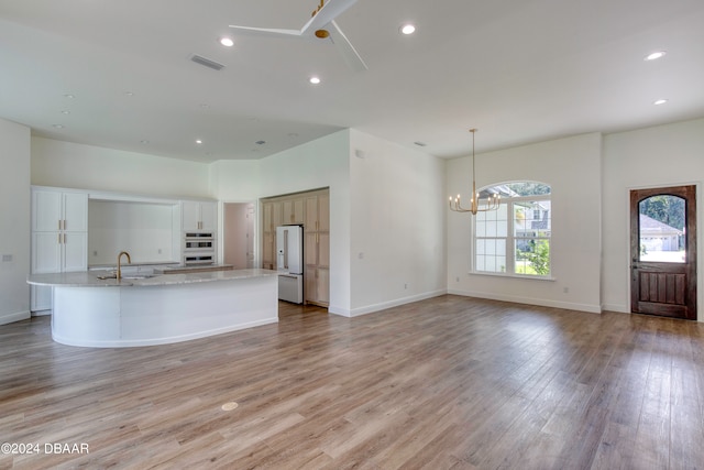 kitchen with a center island with sink, decorative light fixtures, white cabinets, white fridge, and light wood-type flooring