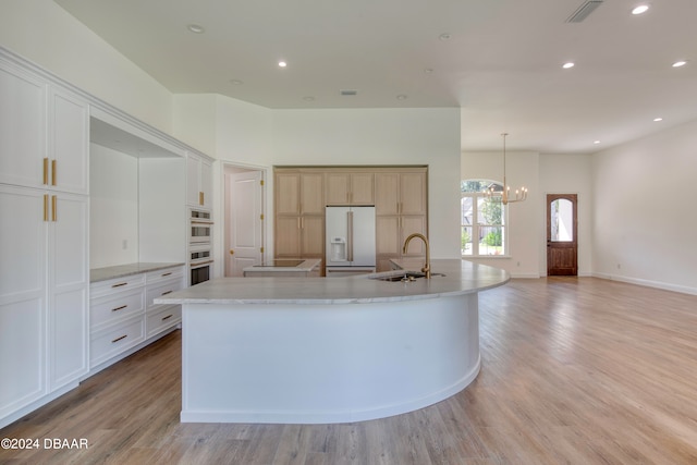 kitchen with a large island, white fridge with ice dispenser, sink, a chandelier, and light hardwood / wood-style flooring