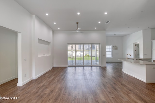 unfurnished living room featuring ceiling fan with notable chandelier, dark wood-type flooring, and a high ceiling