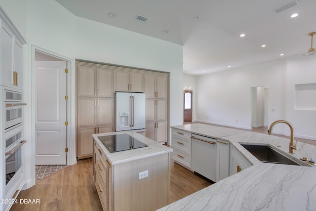 kitchen with light hardwood / wood-style floors, sink, light stone counters, white appliances, and a kitchen island