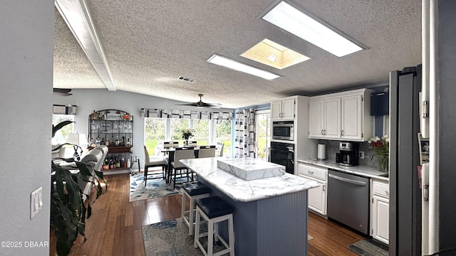 kitchen with dark wood-style flooring, a kitchen island, visible vents, appliances with stainless steel finishes, and lofted ceiling with skylight