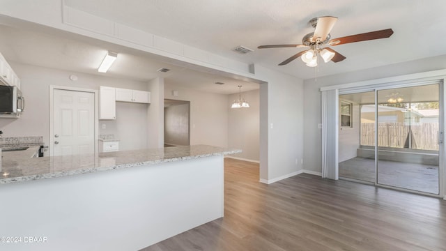 kitchen featuring kitchen peninsula, light stone counters, white cabinets, and ceiling fan with notable chandelier