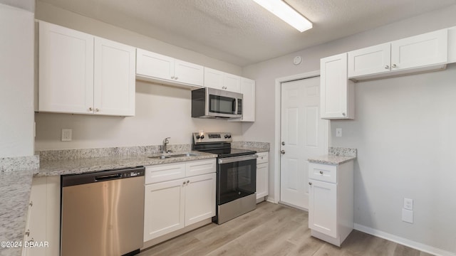 kitchen featuring a textured ceiling, stainless steel appliances, white cabinetry, and light stone counters