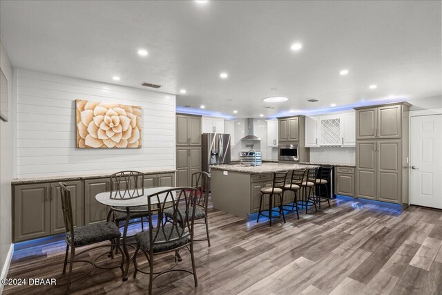 kitchen featuring stainless steel appliances, hardwood / wood-style flooring, wall chimney range hood, a kitchen island, and a breakfast bar