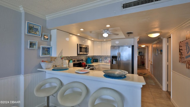 kitchen with stainless steel appliances, white cabinets, kitchen peninsula, decorative backsplash, and light tile patterned floors