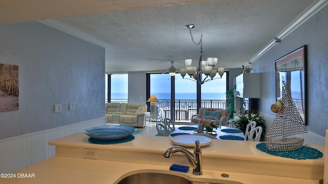 kitchen with ceiling fan with notable chandelier, a water view, a textured ceiling, sink, and ornamental molding