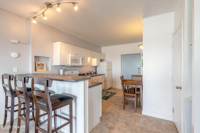 kitchen featuring white cabinetry, sink, a kitchen breakfast bar, kitchen peninsula, and white appliances