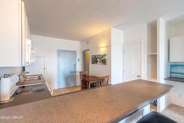 kitchen with sink, kitchen peninsula, stove, a textured ceiling, and white cabinets