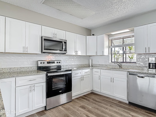 7 Heather Ln, Ormond Beach, FL 32174 - kitchen with stainless steel appliances, a sink, a textured ceiling, white cabinetry, and light wood finished floors