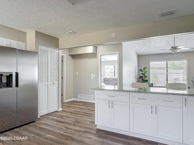 7 Heather Ln, Ormond Beach, FL 32174 - kitchen with stainless steel refrigerator with ice dispenser, a textured ceiling, white cabinets, wood finished floors, and plenty of natural light