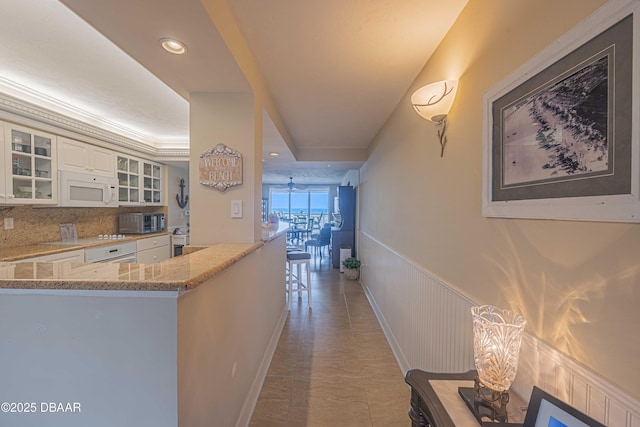 kitchen with decorative backsplash, light stone countertops, white cabinetry, and a tray ceiling