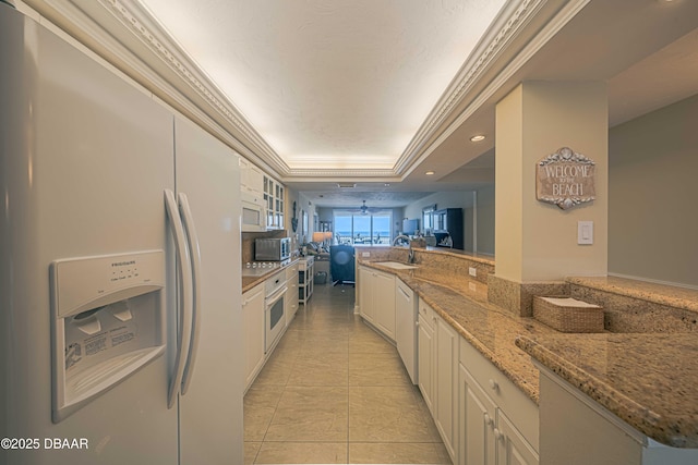 kitchen with white appliances, white cabinetry, sink, light tile patterned flooring, and a tray ceiling