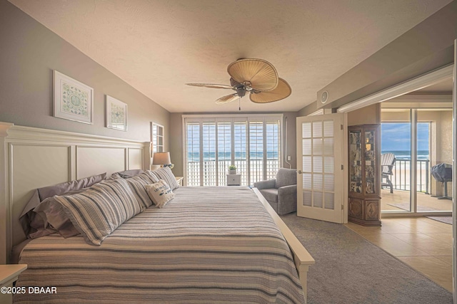 tiled bedroom with ceiling fan, access to exterior, a textured ceiling, and a water view