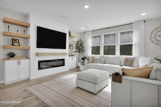 living room with a large fireplace, light hardwood / wood-style flooring, and built in shelves