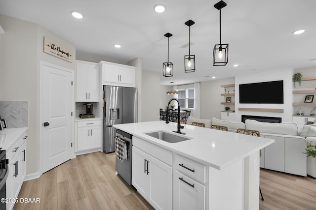 kitchen with a center island with sink, appliances with stainless steel finishes, pendant lighting, white cabinets, and sink