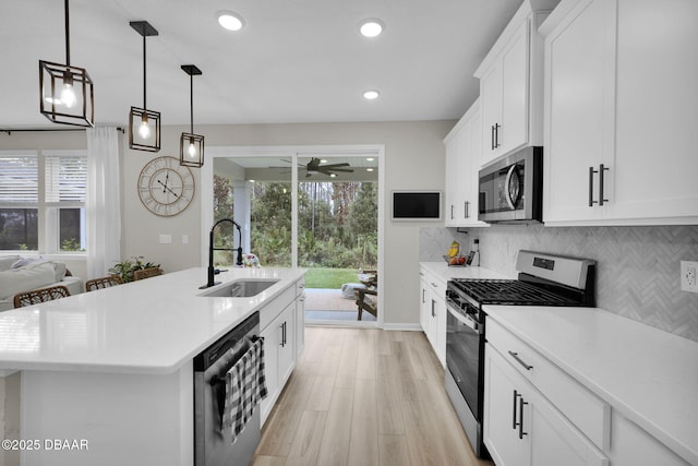 kitchen featuring white cabinets, appliances with stainless steel finishes, an island with sink, sink, and hanging light fixtures