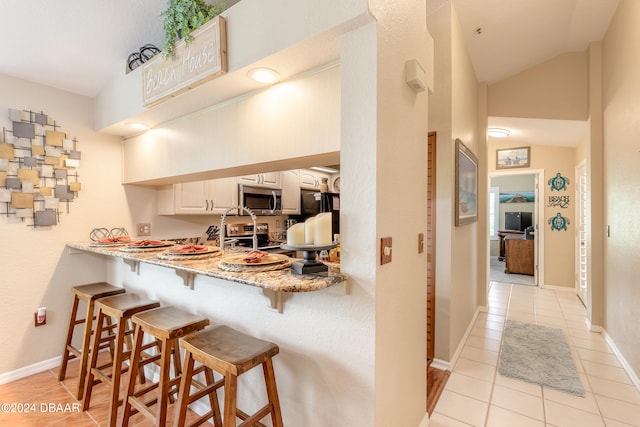 kitchen featuring stainless steel appliances, a kitchen breakfast bar, light stone countertops, light tile patterned floors, and white cabinets