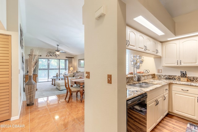 kitchen with light stone counters, dishwasher, sink, ceiling fan, and vaulted ceiling with skylight