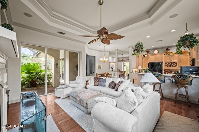 living room with ornamental molding, ceiling fan with notable chandelier, dark hardwood / wood-style floors, and a tray ceiling