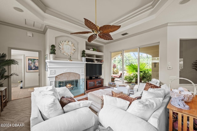 living room with built in shelves, ceiling fan, a tile fireplace, and ornamental molding