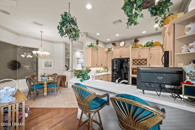 kitchen featuring black appliances, ornamental molding, a notable chandelier, light brown cabinetry, and light hardwood / wood-style flooring