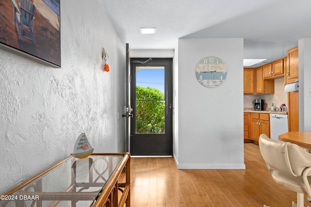 kitchen with white dishwasher, ventilation hood, a textured ceiling, and light wood-type flooring