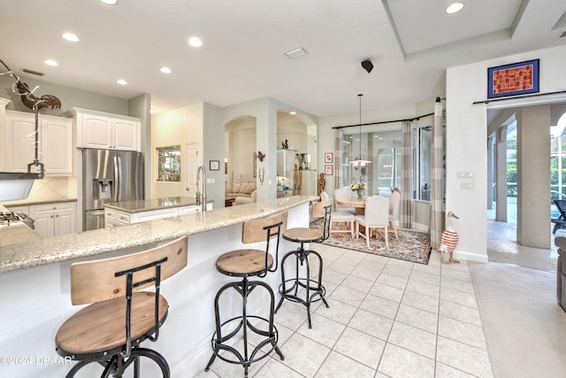 kitchen featuring a center island with sink, stainless steel fridge, light stone countertops, decorative backsplash, and white cabinets