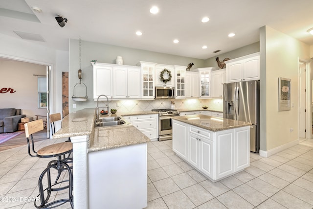 kitchen with light stone counters, sink, a breakfast bar area, white cabinetry, and appliances with stainless steel finishes