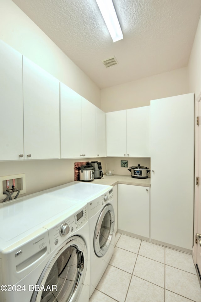 laundry area with cabinets, washing machine and dryer, a textured ceiling, and light tile patterned flooring