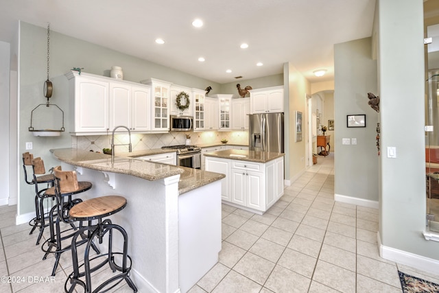 kitchen featuring white cabinets, kitchen peninsula, appliances with stainless steel finishes, and tasteful backsplash