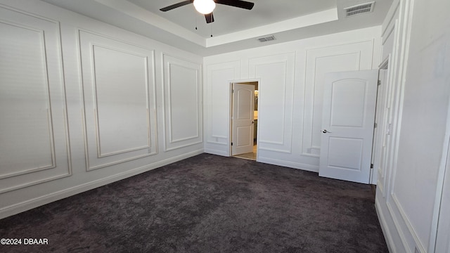 unfurnished bedroom with dark colored carpet, ceiling fan, and a raised ceiling