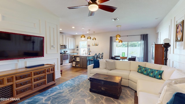 living room with a textured ceiling, ceiling fan, sink, and dark hardwood / wood-style floors