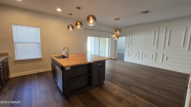 kitchen with a center island with sink, sink, decorative light fixtures, dark hardwood / wood-style flooring, and butcher block counters